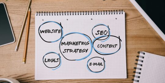 top view of business supplies, digital devices and notebook with marketing strategy on workplace